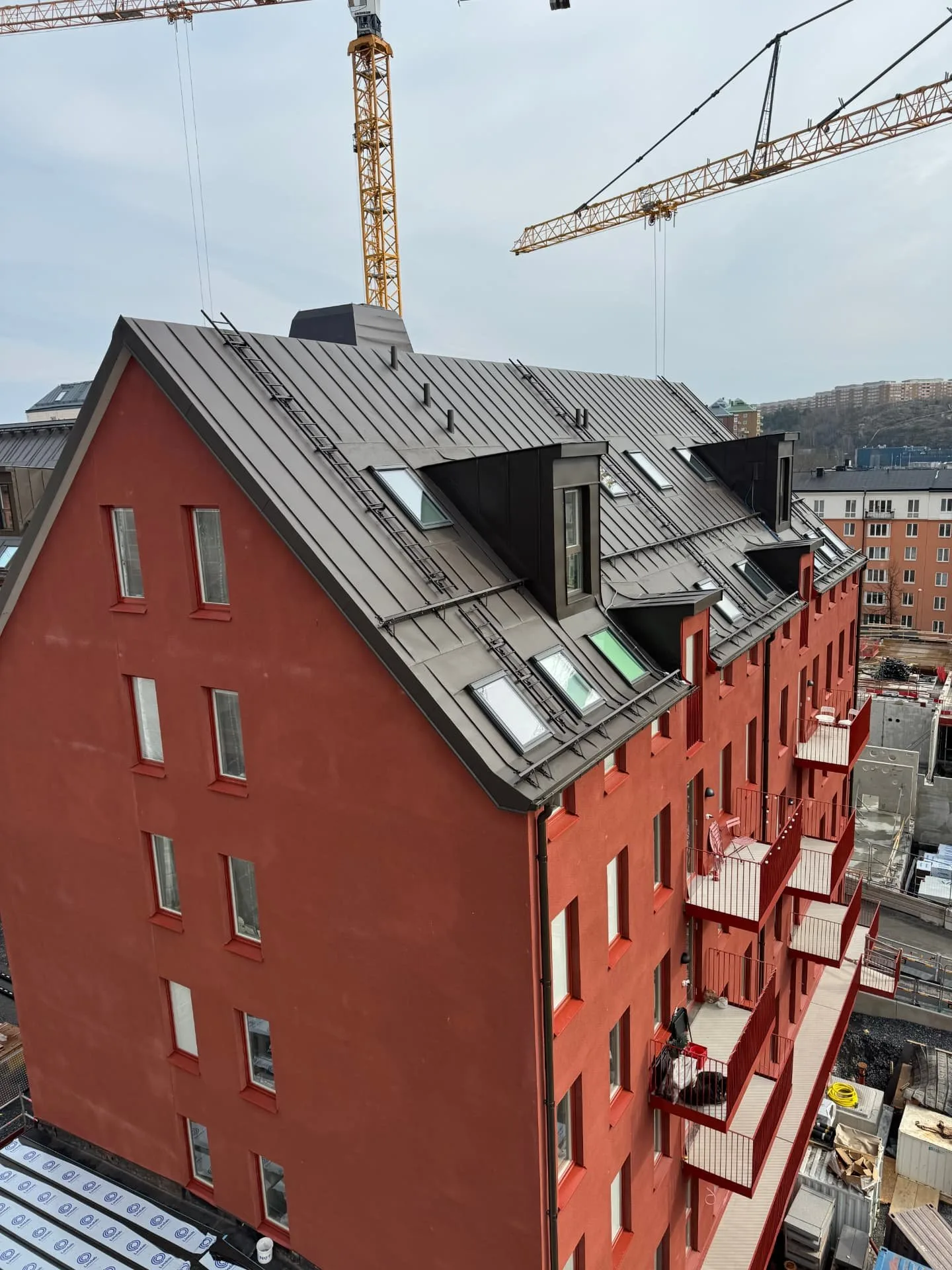 Högt rött flerbostadshus med grått plåttak och takfönster